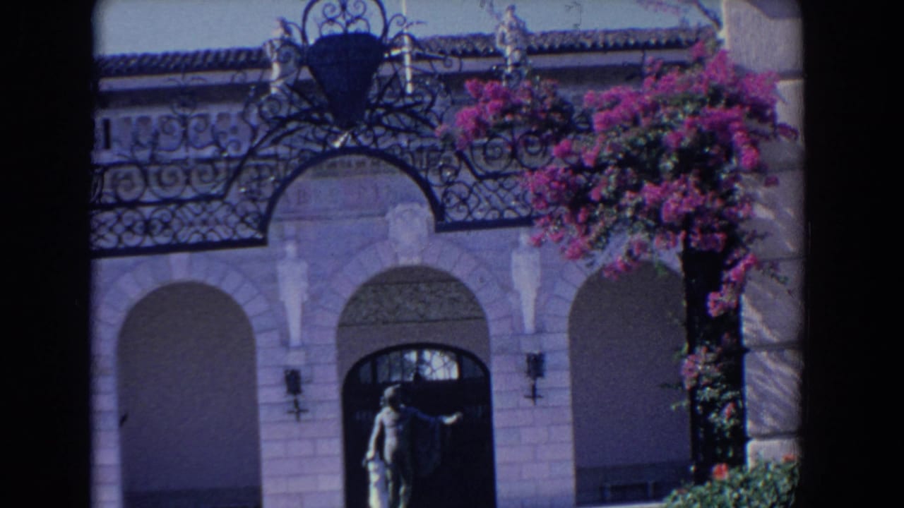 Building facade with arched entry, statue, wrought iron, and bougainvillea.