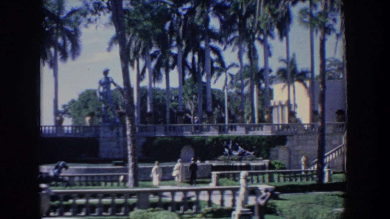 1958 Florida 8mm view of palms, stone terraces, statues, and a white stucco building with arched details.