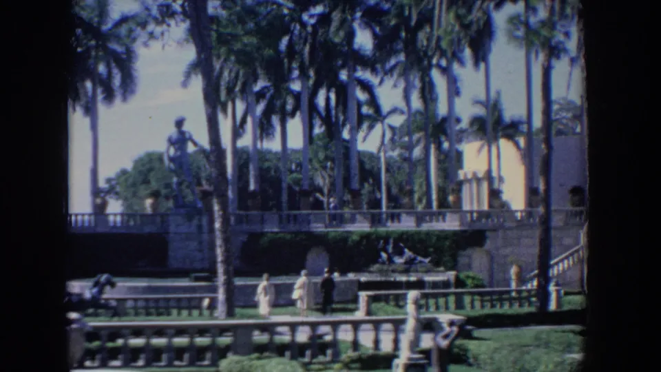 1958 Florida 8mm view of palms, stone terraces, statues, and a white stucco building with arched details.
