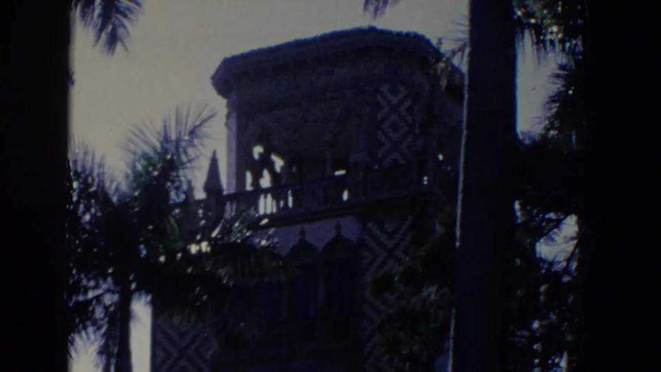1958 Florida 8mm frame of an ornate estate tower or pavilion behind palms, with patterned walls and a shadowed foreground edge.