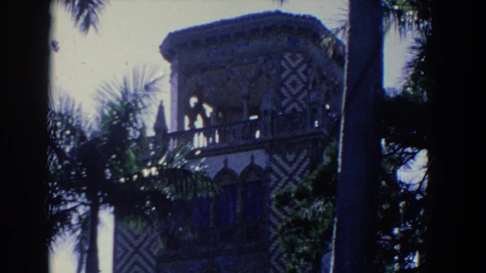 1958 Florida home-movie frame showing a patterned estate tower or pavilion with palms, stone railings, and high-contrast 8mm exposure.