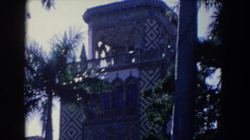 1958 Florida 8mm frame showing a Moorish-style patterned building exterior behind palm trunks and tropical foliage.