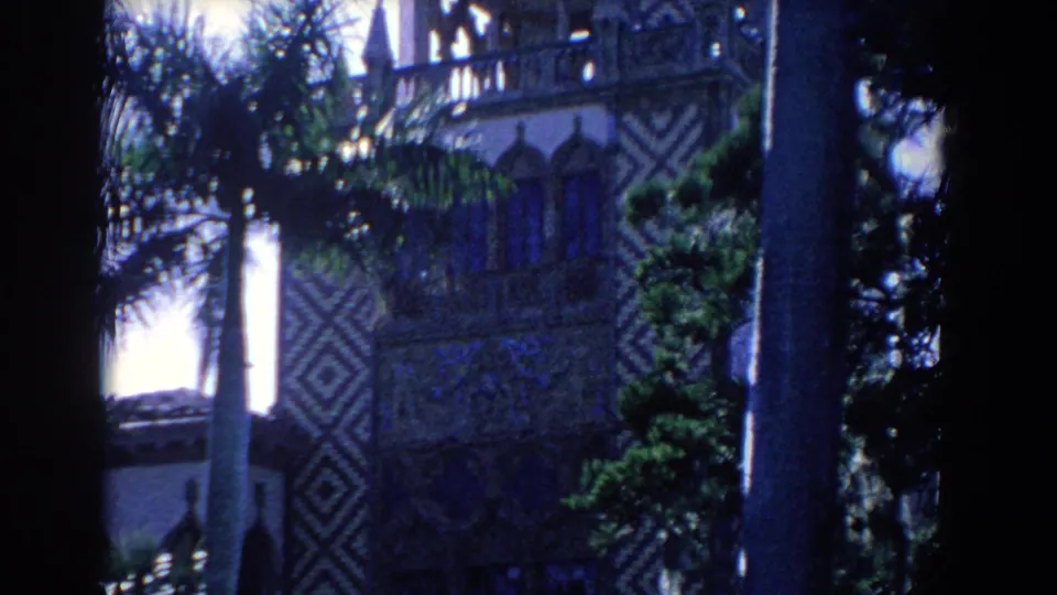 1958 Florida 8mm frame showing the ornate building exterior from below, with palms, shrubs, and geometric wall patterns.