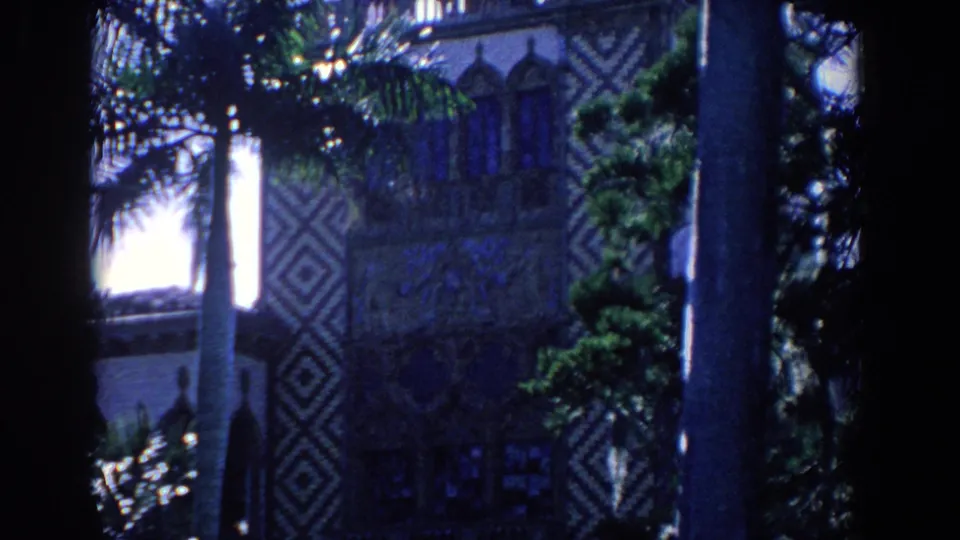1958 Florida 8mm frame of a patterned Moorish-style exterior, arched window openings, palms, and a dark foreground trunk.