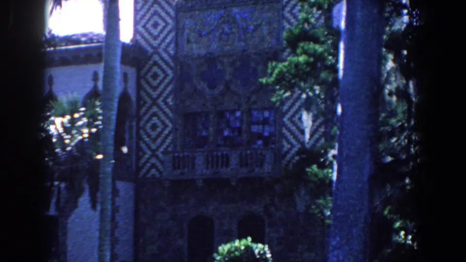 1958 Florida 8mm frame showing an ornate exterior with arched openings, palm trunks, greenery, and decorative geometric facade work.