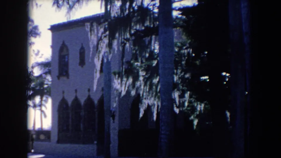 1958 Florida 8mm frame showing palms and Spanish moss in front of a light-colored Gothic-style building exterior.