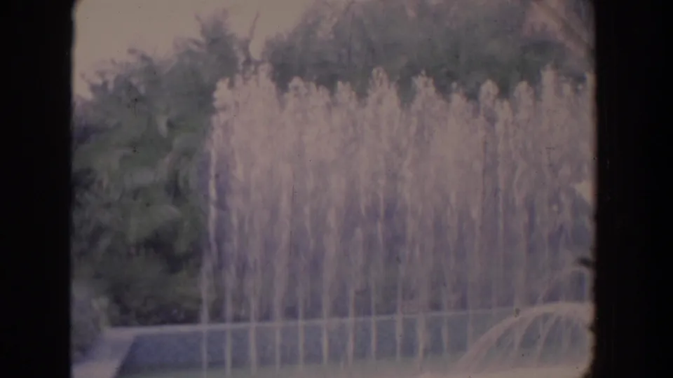 A Florida outdoor fountain sprays upward in home-movie footage, backed by trees and landscaping.