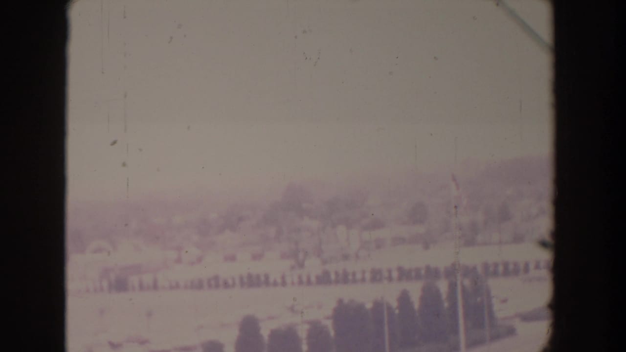 Hazy distant landscape with fields, trees, and pale sky seen through an 8mm film frame.
