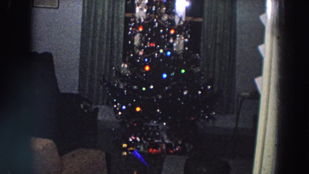 Lit Christmas tree beside dark curtains and chairs in a living room.