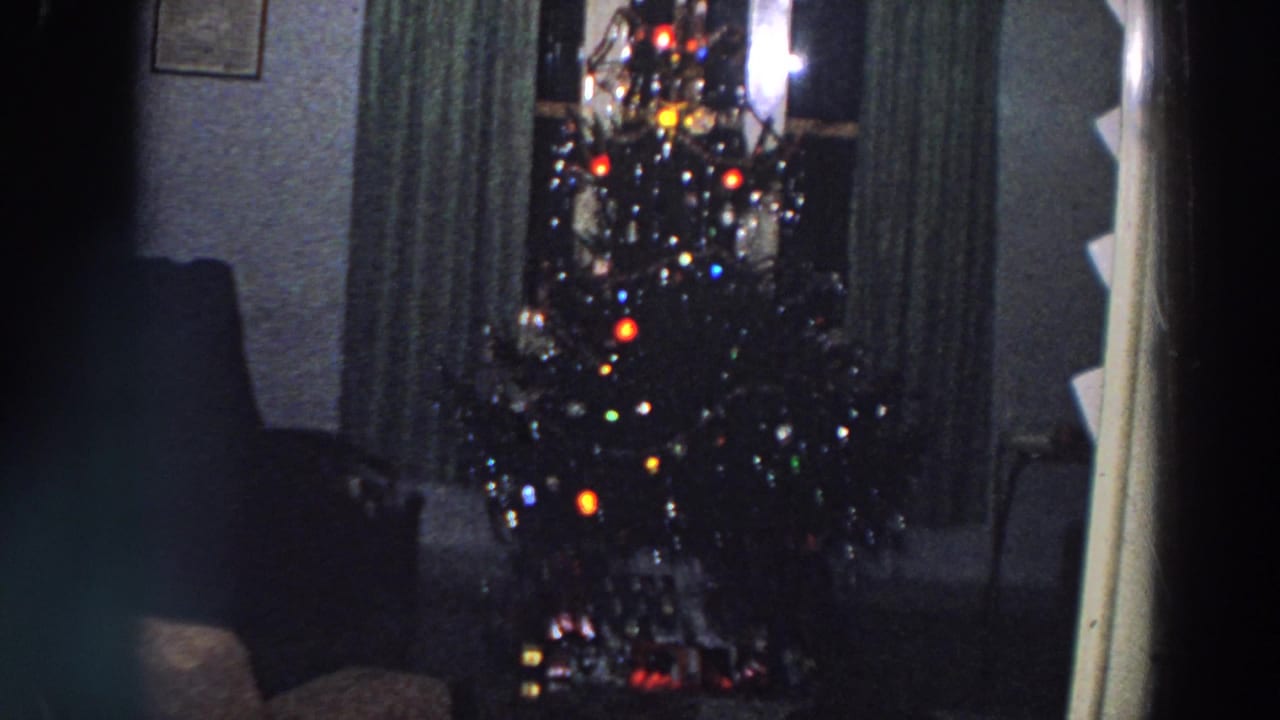 Lit Christmas tree framed by curtains with dark seating nearby.