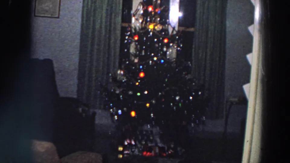 1958 Italy home-movie view of a decorated Christmas tree with multicolored lights, curtains, and shadowed living-room furniture.