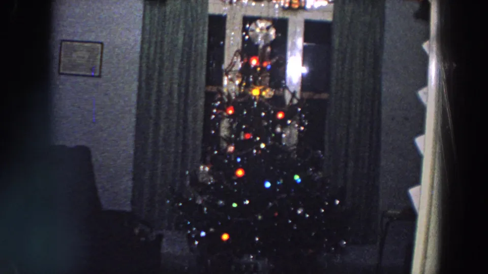 1958 Italy domestic interior with a decorated Christmas tree, silver tinsel, colored lights, curtains, and a small framed picture on the wall.