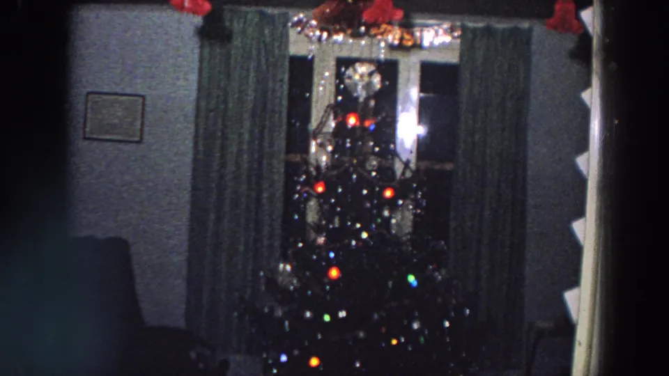 1958 Italy frame showing a lit Christmas tree with ornaments and tinsel in a dim living room with curtains and nearby furniture.