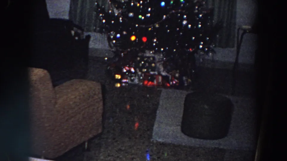 1958 Italy home-movie frame of a Christmas tree with colored lights and gifts beneath it in a private living room.