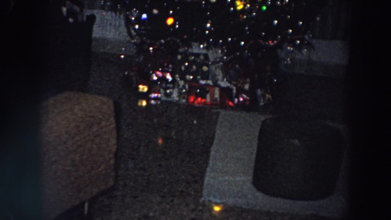 1958 Italian 8mm frame showing a low-lit Christmas tree with colored lights and gifts in a private living room.