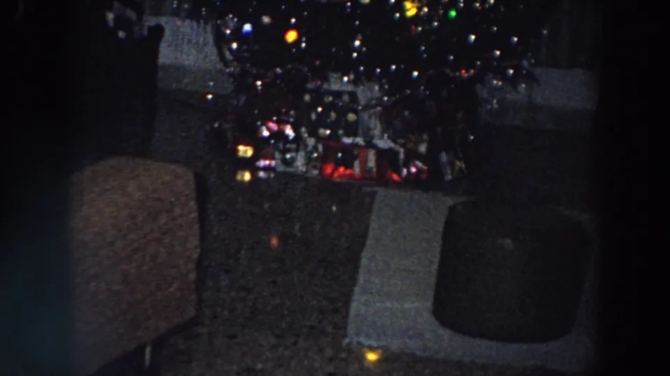 1958 Italian 8mm frame showing a low-lit Christmas tree with colored lights and gifts in a private living room.