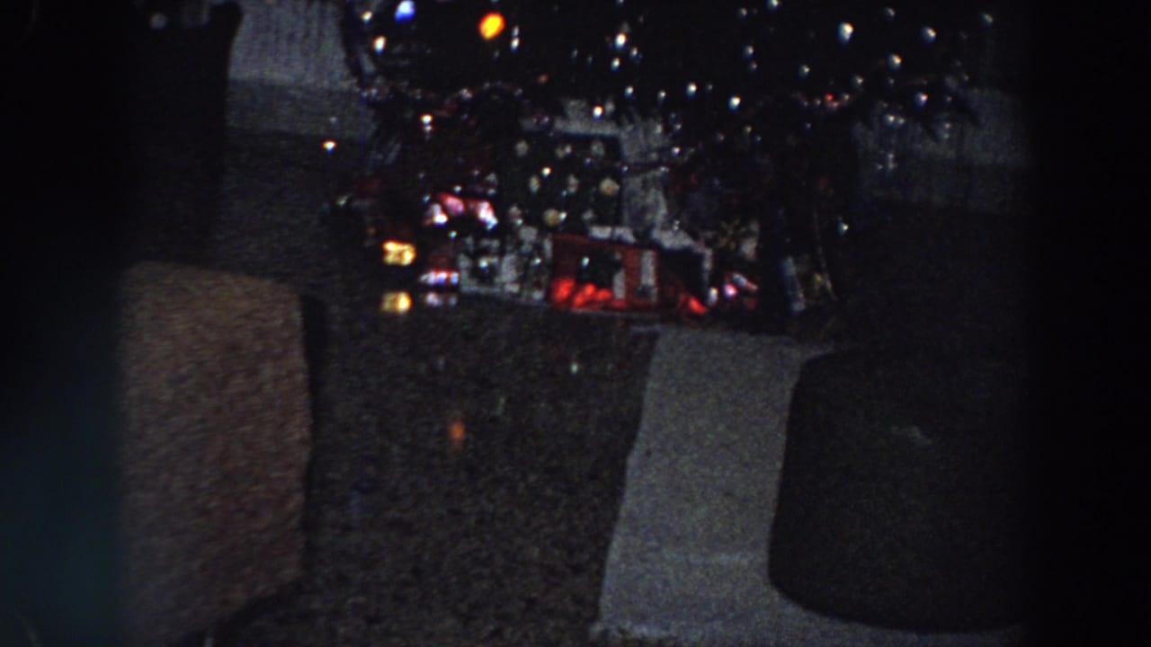 Decorated Christmas tree with glowing lights and presents beside dark furniture.