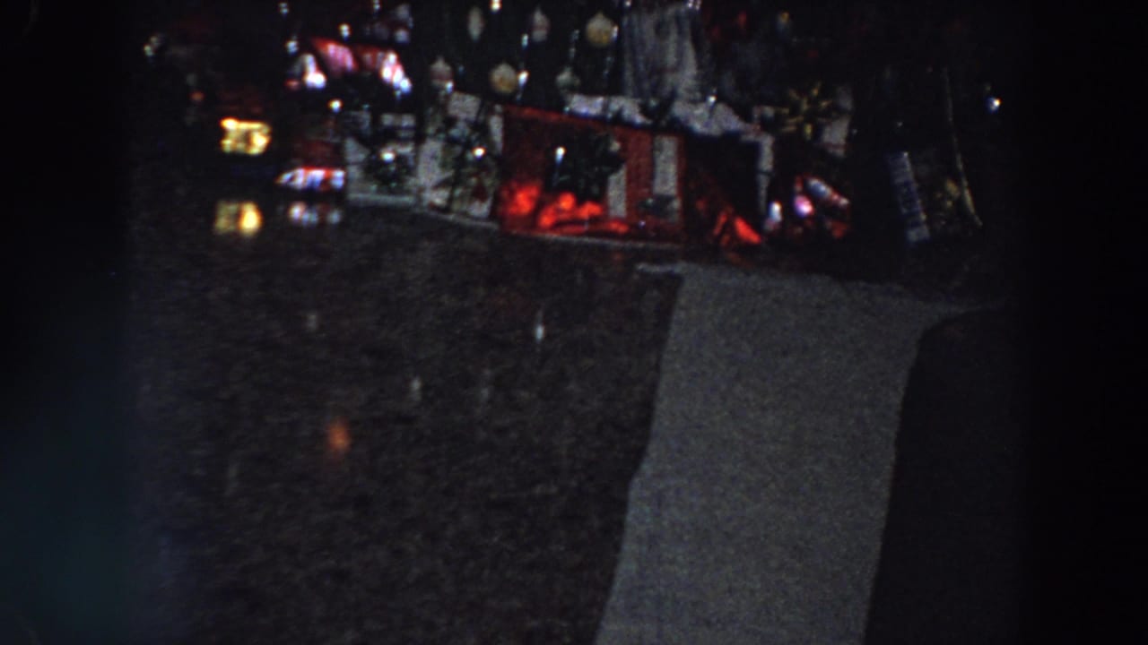 Dim 1958 Italy 8mm frame showing a dark tabletop area and indistinct household objects before the camera turns toward the decorated door.
