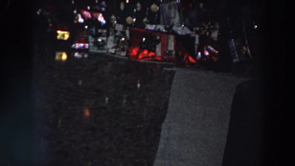 Dim 1958 Italy 8mm frame showing a dark tabletop area and indistinct household objects before the camera turns toward the decorated door.