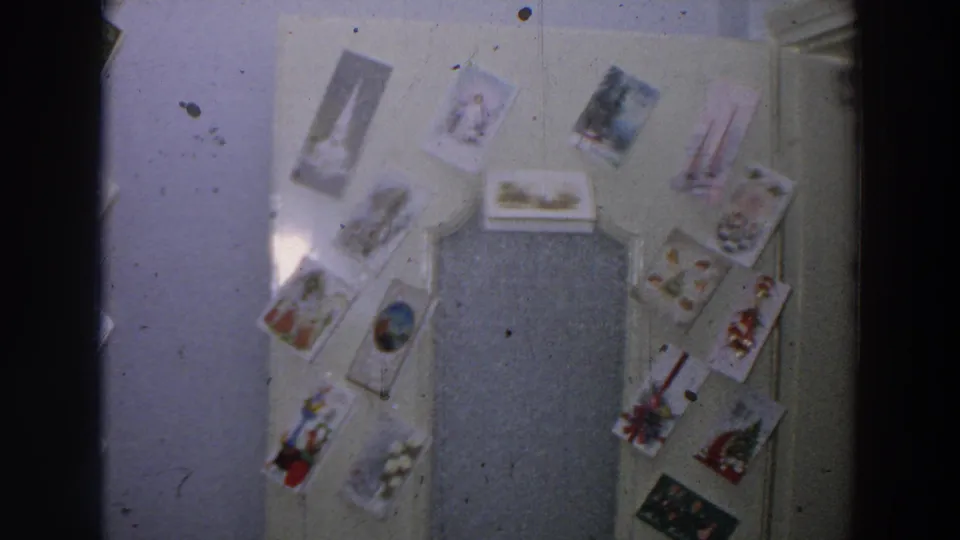 1958 Italy home-movie frame showing a pale door covered with postcards, including winter or religious holiday-style imagery.