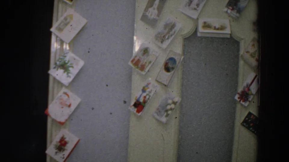 Christmas cards remain visible on a pale wall beside a closed interior door in this 1958 Italy home-movie frame.
