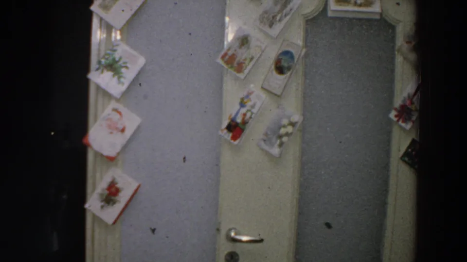 A handheld 8mm view shows greeting cards around a doorway, with the lower door handle visible in a domestic Italian interior.