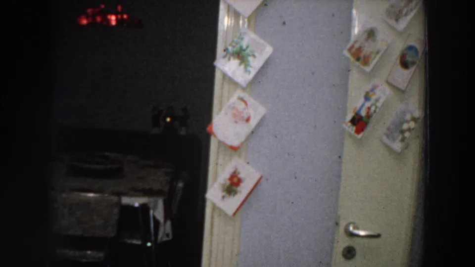 Christmas cards frame the doorway while a dim dining area with a table and red light appears beyond in the 1958 home interior.