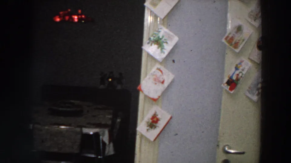 Low-light 8mm frame from Italy in 1958 showing holiday cards on a doorway next to a small dining room.