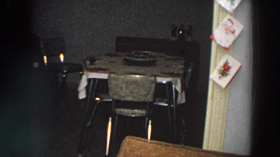 Late-1950s 8mm frame from Italy showing a dim dining room with candles and Christmas cards along the door frame.