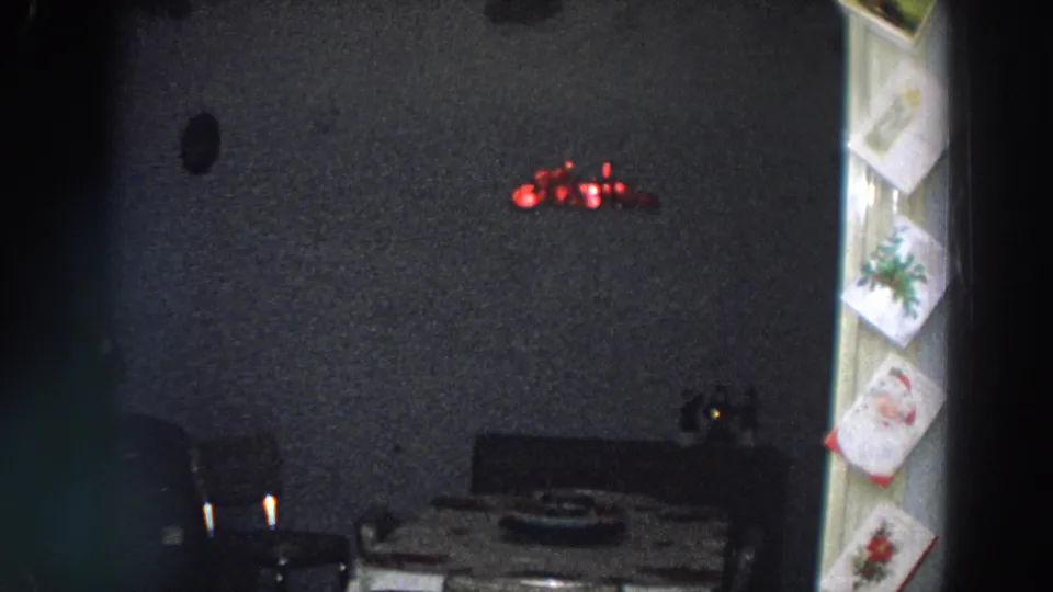 1958 Italy frame of a dark dining-room corner with table and chairs, red wall light, and Christmas cards hanging along the doorway.