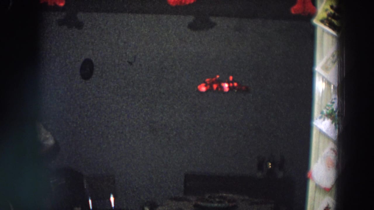 Dim 1958 Italy home interior with red tinsel on a dark wall and furniture edges partly visible.
