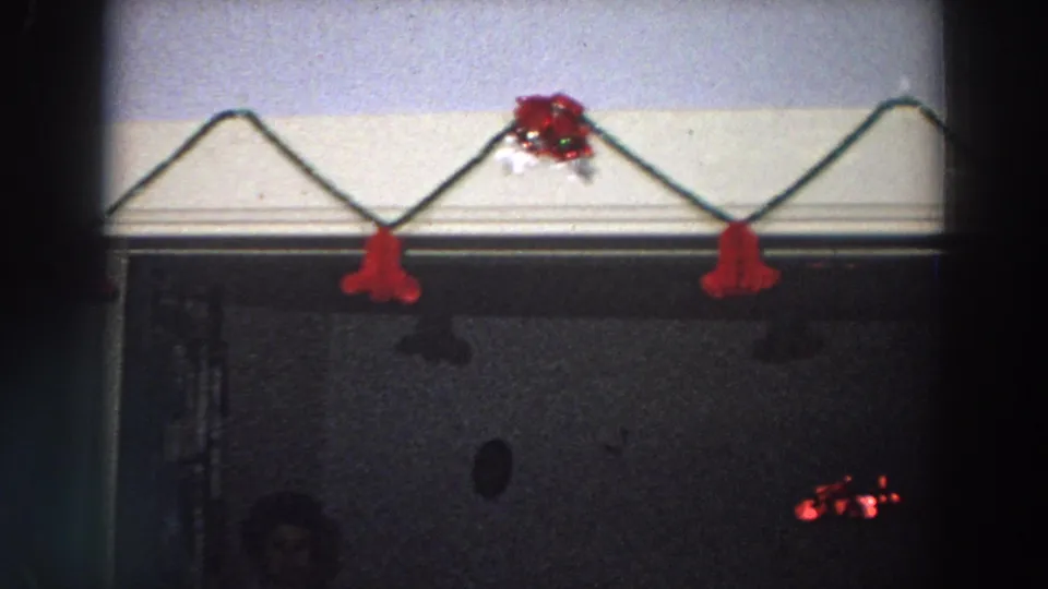 1958 Italy 8mm frame showing red Christmas decorations above a dark doorway, with a faint person partly visible in the lower area.