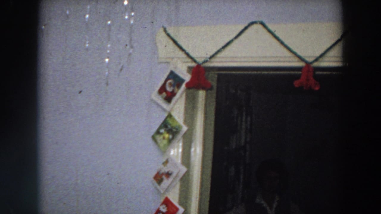 1958 Italy home-movie frame showing red Christmas garland over a doorway and greeting cards taped vertically along the wall.