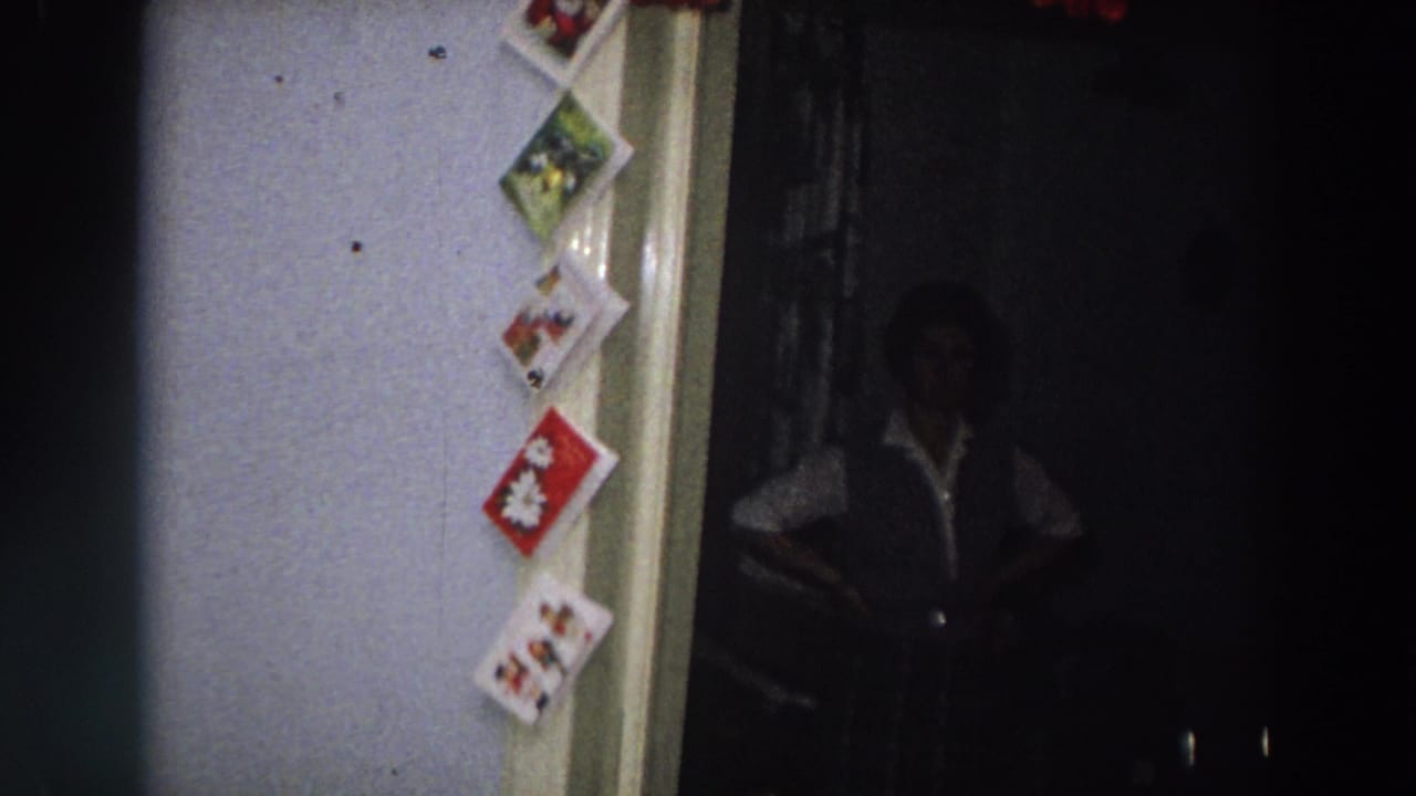 1958 Italy home-movie frame showing Christmas cards beside a doorway, with a partially silhouetted person standing in the dim interior.