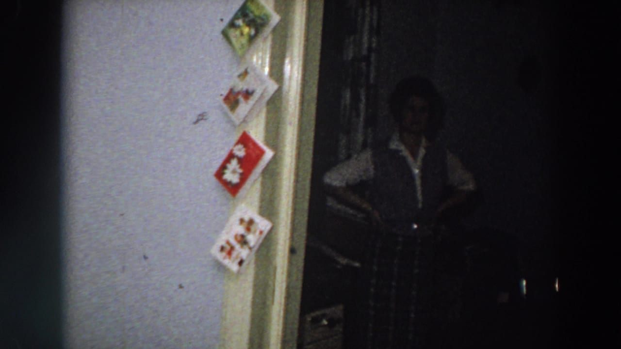 1958 Italy frame with a person in a dark vest and light shirt standing in a dim doorway beside a vertical display of Christmas cards.