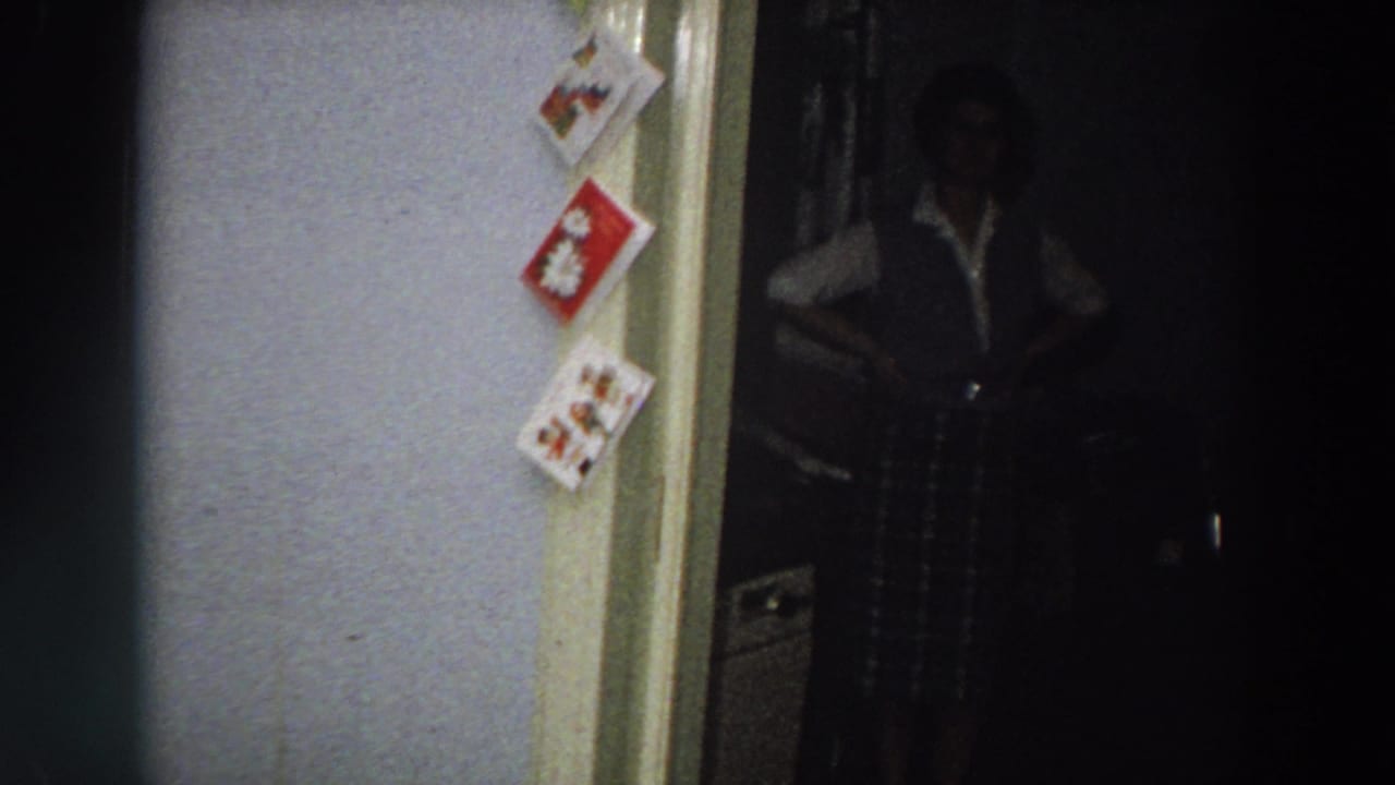 Dim bedroom doorway with Christmas cards on the wall and a woman partly visible in shadow.
