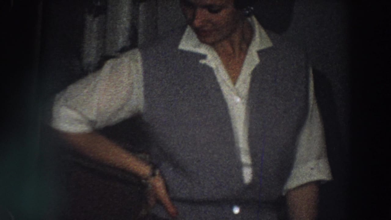 1958 Italy home-movie frame of an adult woman in a white collared shirt and grey vest posing indoors in low light.