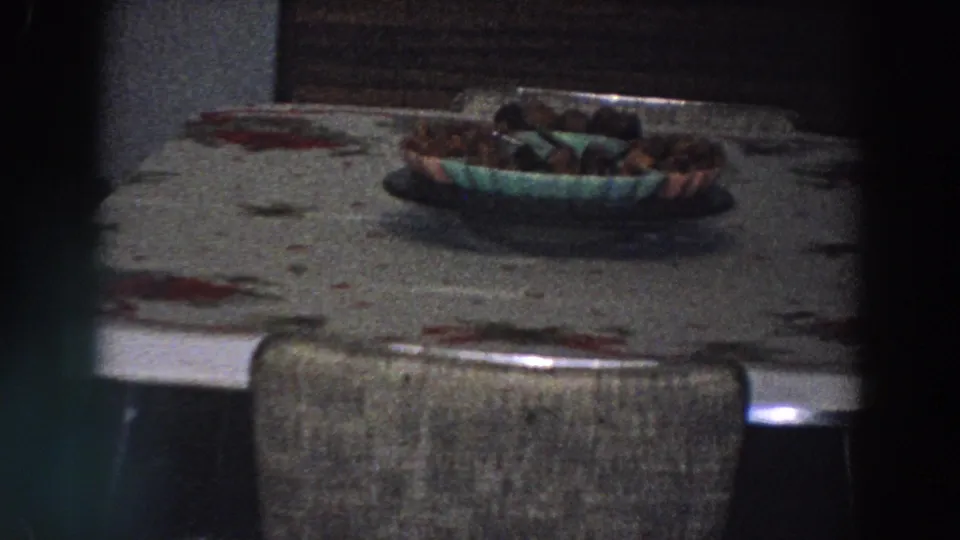 A dining table in the Italian home shows a floral tablecloth, upholstered chair, and bowl of food under low indoor light.