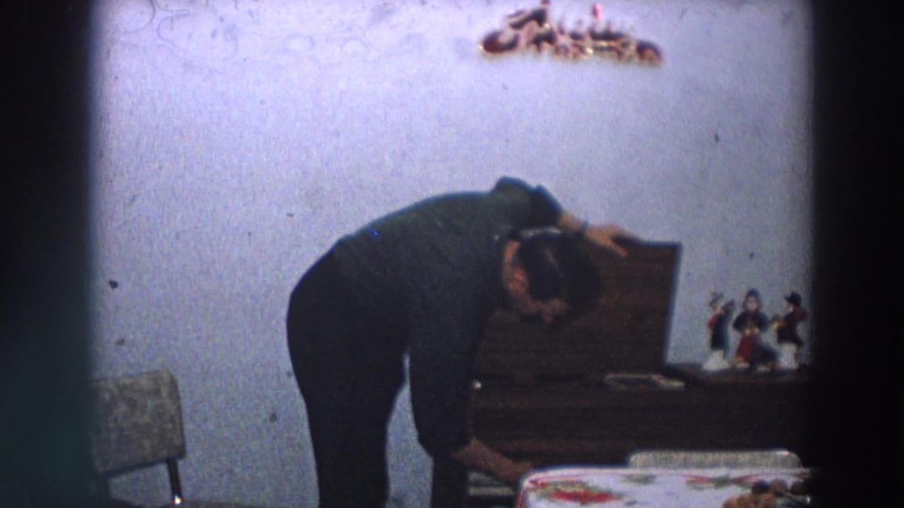 An adult man bends over a wooden cabinet in a 1958 Italian home, with small figurines and wall decoration nearby.