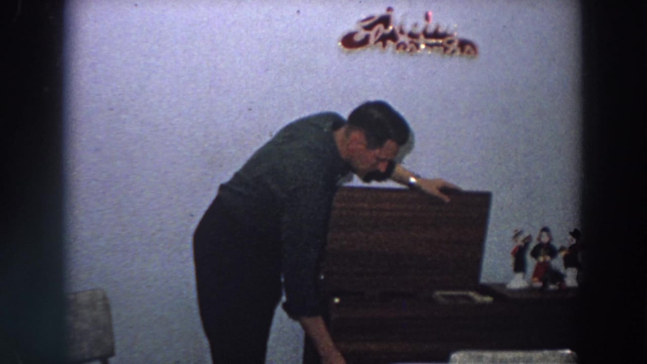 The man remains bent near the cabinet and dining table, suggesting household preparation in the Italian home interior.