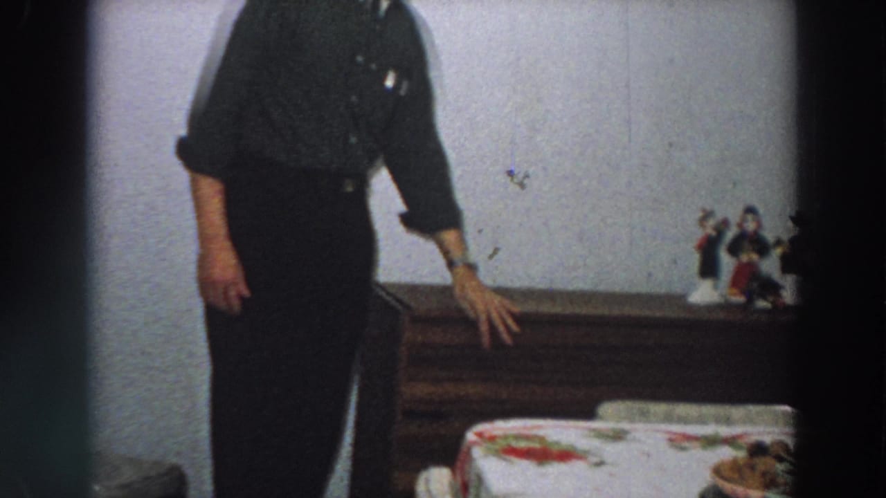 The man rests a hand near the wooden box while a bed edge and small figurines appear in the 1958 Italy home interior.