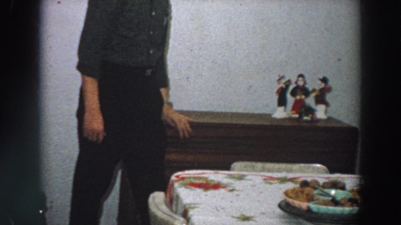 In a 1958 Italian home interior, an adult man stands partly cropped beside a floral-covered dining table and wooden dresser.
