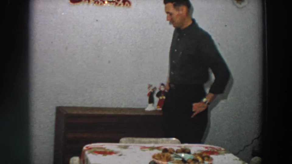 The man looks down while standing beside the dining table in a private 1958 Italian home interior.