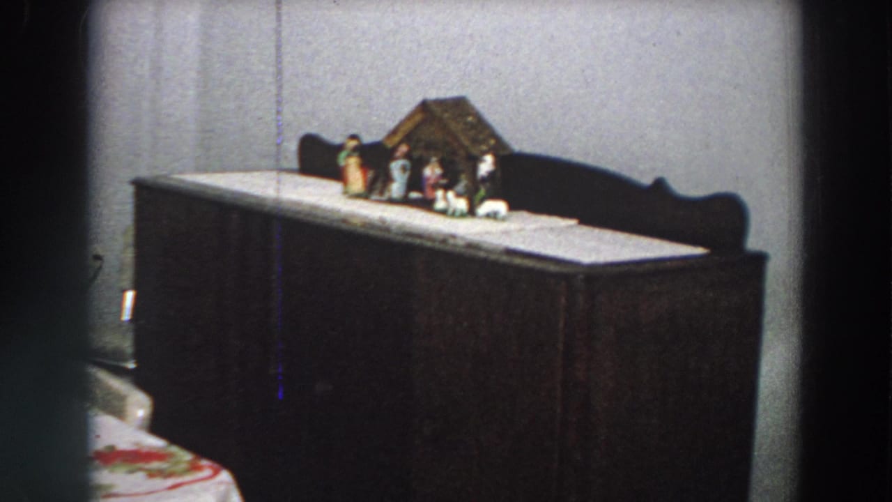 1958 Italian home-movie view of a dark cabinet topped with a nativity display, with a floral tablecloth visible at left.