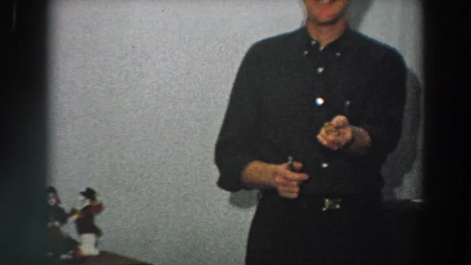 In a softly focused 1958 Italy interior, the man lifts one hand as if showing or inspecting a small item.