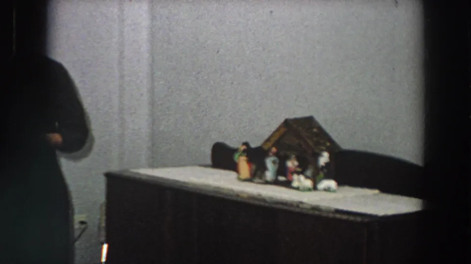 A small nativity arrangement with several figurines sits on a cabinet or table in a plain interior, shown in 1958 Italy home-movie footage.