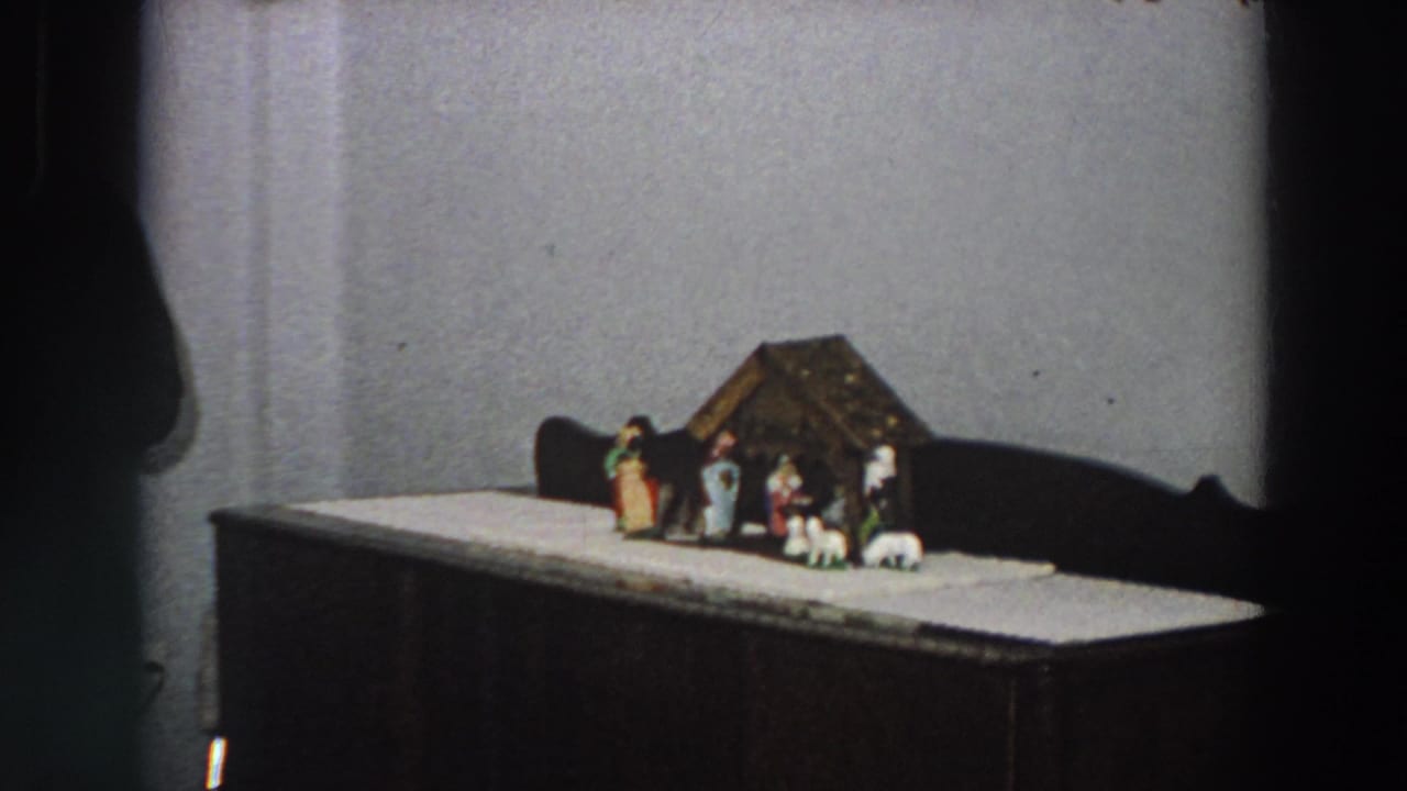 1958 Italy home-movie frame showing a small Christmas nativity set on a cabinet against a plain wall.