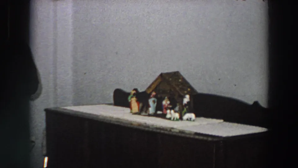 1958 Italy home-movie frame showing a small Christmas nativity set on a cabinet against a plain wall.