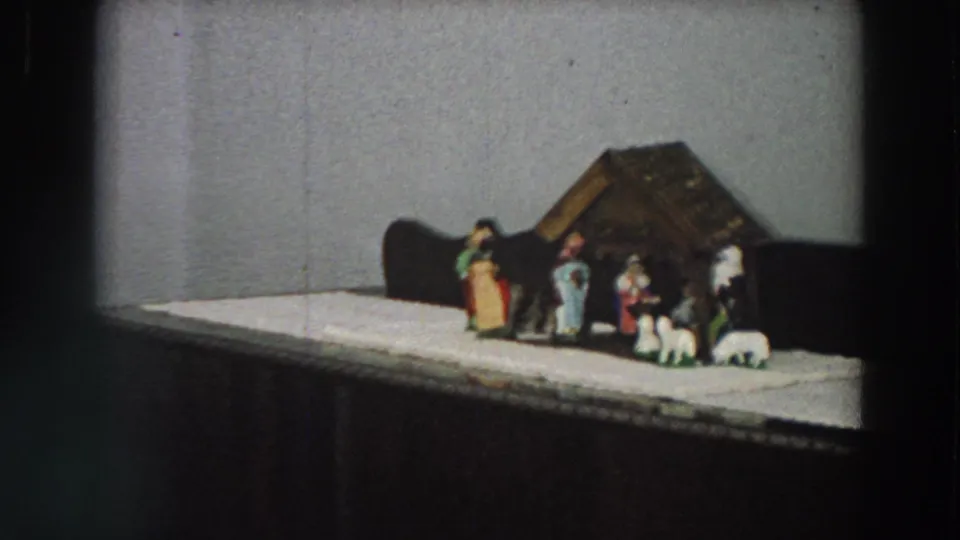 1958 Italy home-movie still showing a closer view of a small nativity scene on a white cloth-covered cabinet.