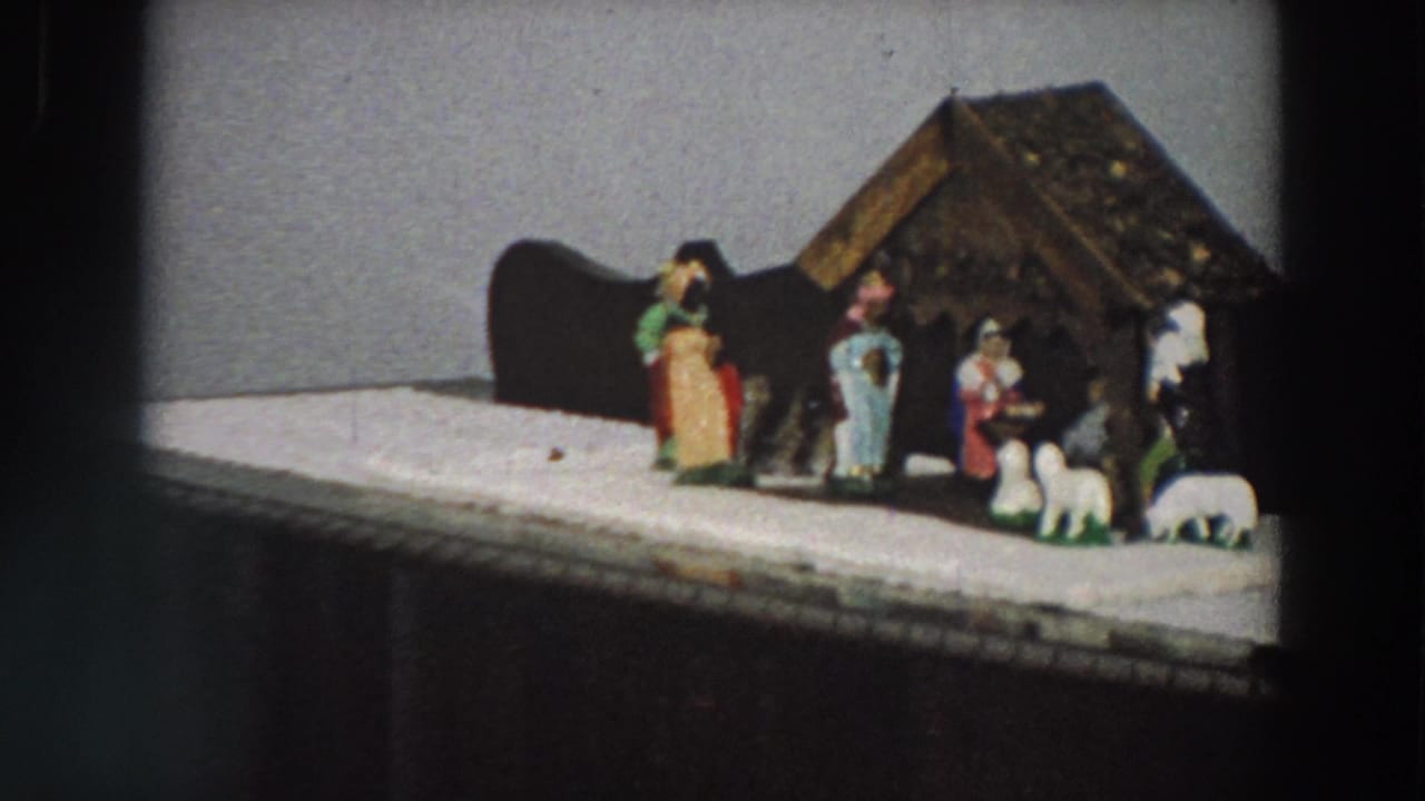 1958 Italy home-movie frame showing a tabletop Christmas nativity scene with small figures and sheep on a white-covered cabinet.